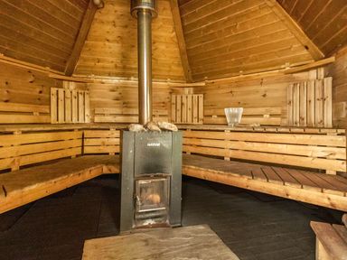 A wooden sauna with bench seating and a central stove at Eden Lodge in Bardsea