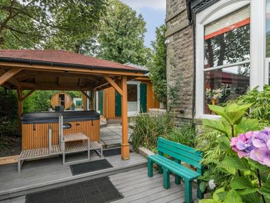 An outdoor area with a covered hot tub a green bench plants and a window of a stone building at Eden Lodge in Bardsea