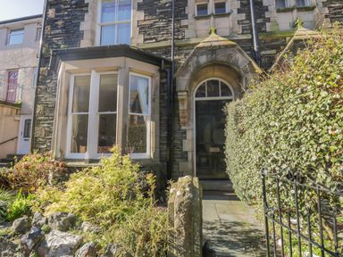 A stone house exterior with an arched doorway and bay window surrounded by bushes and a metal gate at 48 Oak Street in Windermere