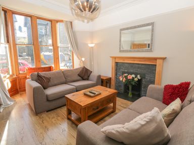 A living room with two sofas a wooden coffee table a fireplace with flowers and a large window at 48 Oak Street in Windermere