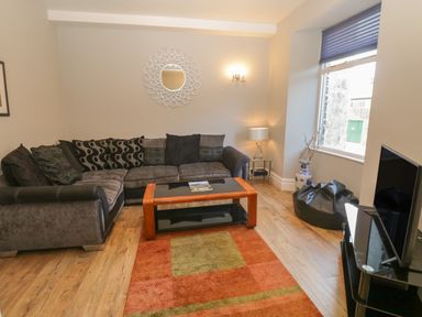 A living room with a sectional sofa a coffee table a TV on a stand a window and a rug at 48 Oak Street in Windermere