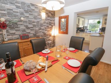 A dining room with a wooden table set with plates glasses and bread with a view into a white kitchen at 48 Oak Street in Windermere