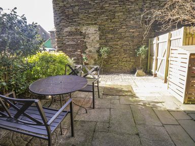 A patio with a round metal table and metal chairs near a stone wall and wooden fence at 48 Oak Street in Windermere