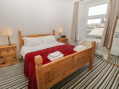 A bedroom with a wooden bed frame red blanket striped carpet and two bedside tables with lamps at 48 Oak Street in Windermere