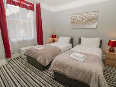 A bedroom with two single beds bedside tables with lamps red curtains and a striped carpet at 48 Oak Street in Windermere