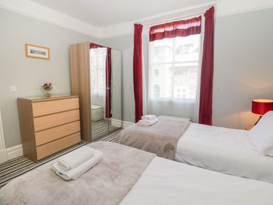 A bedroom with two beds a wooden dresser a mirrored wardrobe and red curtains at 48 Oak Street in Windermere