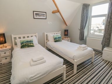 A bedroom with two single beds white framed beds bedside tables lamps and a window at 48 Oak Street in Windermere