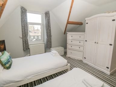 A bedroom with two single beds a window with grey curtains a white chest of drawers and a white wardrobe at 48 Oak Street in Windermere