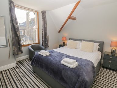 A bedroom with a double bed with pillows and folded towels two bedside tables with lamps a chair next to a window with curtains a striped carpet at 48 Oak Street in Windermere