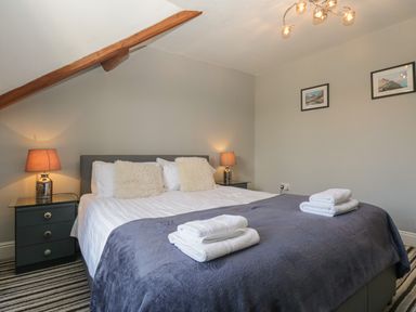 A bedroom with a double bed two bedside tables with lamps folded towels on the bed and two framed pictures on the wall at 48 Oak Street in Windermere