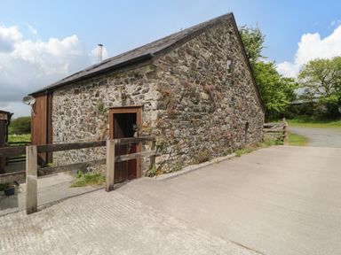 An exterior view of a stone barn with a wooden door a wooden railing and a driveway at Meader Barn Peter Tavy near Tavistock