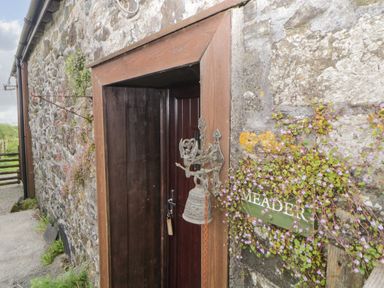 A wooden door with a metal bell and a green sign reading Meader on a stone wall at Meader Barn Peter Tavy near Tavistock