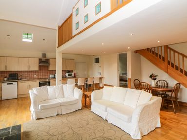 An open plan living room with two white sofas a round wooden dining table with chairs wooden staircase and kitchen at Meader Barn Peter Tavy near Tavistock