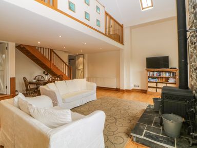 A living room with white sofas and a wood stove next to a bookshelf with a tv above at Meader Barn in Peter Tavy near Tavistock