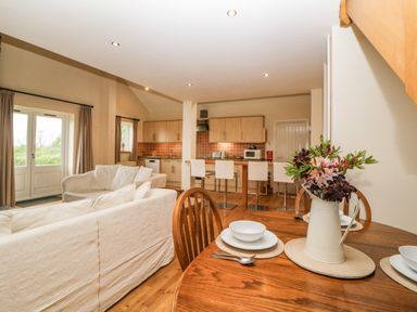 An open plan living area with a dining table set with dishes a flower vase on the table white sofas kitchen cabinets and bar stools at Meader Barn Peter Tavy near Tavistock