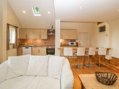 A kitchen and dining area with wooden cabinets white chairs a white sofa and a wooden table at Meader Barn Peter Tavy near Tavistock