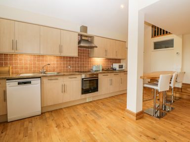 A kitchen with wooden cabinets dishwasher oven toaster microwave and a dining table with chairs at Meader Barn Peter Tavy near Tavistock