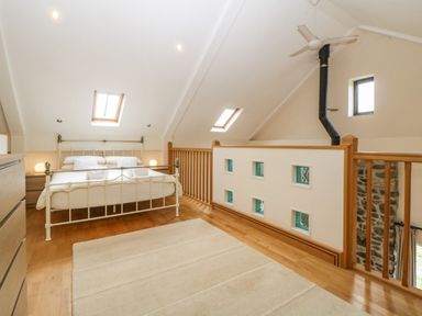 A bedroom with a white metal bed frame wooden floors skylights and a wooden railing at Meader Barn in Peter Tavy near Tavistock