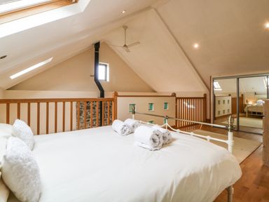 A bedroom with a double bed and rolled towels near wooden railing and mirrored closet at Meader Barn in Peter Tavy near Tavistock