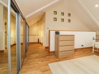 A hallway with wooden floor mirrored sliding closet doors wooden chest of drawers and a rug at Meader Barn in Peter Tavy near Tavistock
