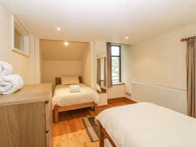 A bedroom with two single beds wooden dresser window with curtains and a wall mirror at Meader Barn in Peter Tavy near Tavistock