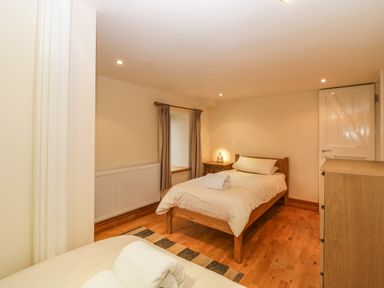 A bedroom with two single beds a wooden chest of drawers a bedside table with a lamp and a window with curtains at Meader Barn in Peter Tavy near Tavistock