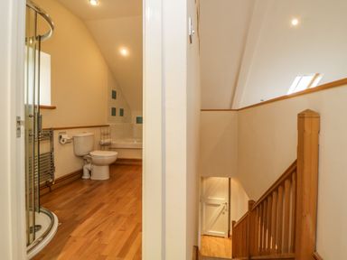 A bathroom with a shower, toilet, and bathtub next to a wooden staircase with a white door at Meader Barn in Peter Tavy near Tavistock