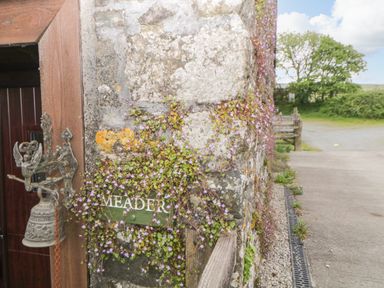 An outdoor stone wall with a green sign reading MEADER and a metal bell hanging next to a wooden door at Meader Barn in Peter Tavy near Tavistock