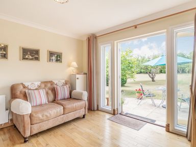 A living room with a sofa pillows and framed pictures next to glass doors leading to a garden at Norbank Garden Studio in Bressingham