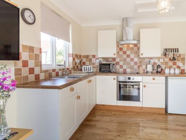 A kitchen with white cabinets wooden countertops tiled backsplash and stainless steel oven at Norbank Garden Studio in Bressingham