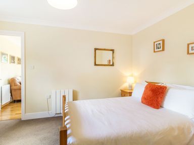A bedroom with a bed featuring white sheets and an orange pillow a wooden nightstand with a lamp and a mirror on the wall at Norbank Garden Studio in Bressingham