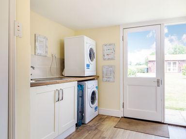 A laundry room with washing machine and dryer under a wooden countertop and a door leading outside at Norbank Garden Studio in Bressingham