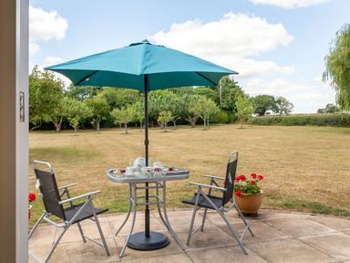 A patio table with tea set and two chairs under a blue umbrella in a garden at Norbank Garden Studio in Bressingham