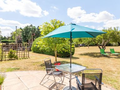 A garden patio with a glass table and two chairs under a blue umbrella at Norbank Garden Studio in Bressingham