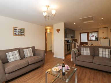 A living room with two brown sofas a glass coffee table and an open kitchen at Roan Cottage in Royal Wootton Bassett