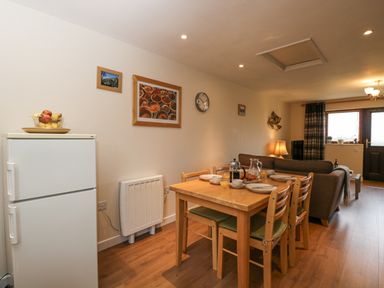 A dining table set for breakfast with plates cups and a coffee pot in a living area with a sofa and refrigerator at Roan Cottage in Royal Wootton Bassett