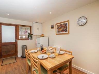 A dining area with a wooden table set with plates and glasses a door and window with blinds in the background at Roan Cottage in Royal Wootton Bassett