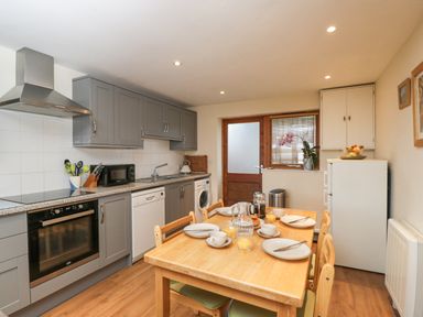 A kitchen with grey cabinets wooden dining table set with plates and cups at Roan Cottage in Royal Wootton Bassett