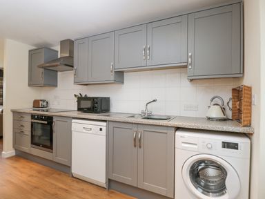 A kitchen with grey cabinets a washing machine dishwasher microwave oven and kettle at Roan Cottage in Royal Wootton Bassett