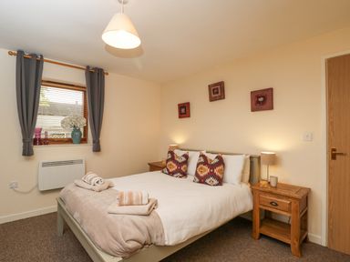 A bedroom with a bed two wooden nightstands and a window with curtains at Roan Cottage in Royal Wootton Bassett