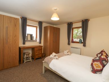 A bedroom with a bed pillows two wardrobes a wooden dressing table with a stool and two windows with curtains at Roan Cottage in Royal Wootton Bassett