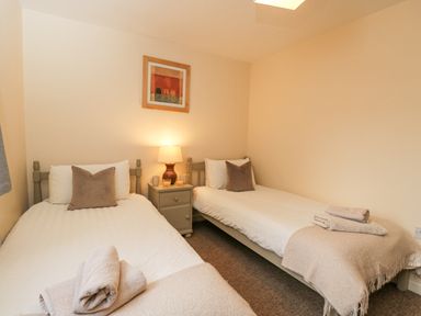A bedroom with two single beds a nightstand with a lamp and folded towels at Roan Cottage in Royal Wootton Bassett