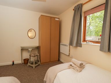 A bedroom with a wooden wardrobe a small table with a stool a window with grey curtains and a bed with towels on it at Roan Cottage in Royal Wootton Bassett