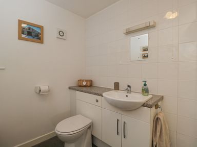 A bathroom with a toilet sink countertop mirror towel and framed picture at Roan Cottage in Royal Wootton Bassett