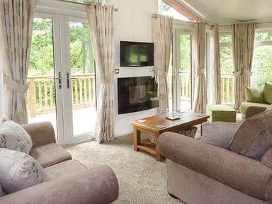 A living room with sofas a wooden coffee table a wall mounted television and glass doors at Chaffinch Lodge in Highampton near Sheepwash
