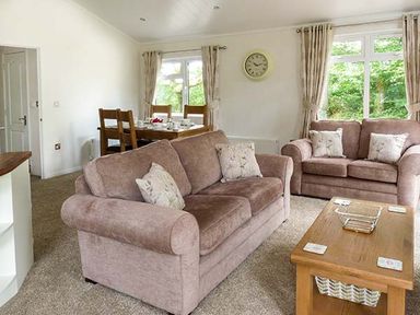 A living room with two brown sofas a wooden coffee table and a dining table with chairs at Chaffinch Lodge in Highampton near Sheepwash