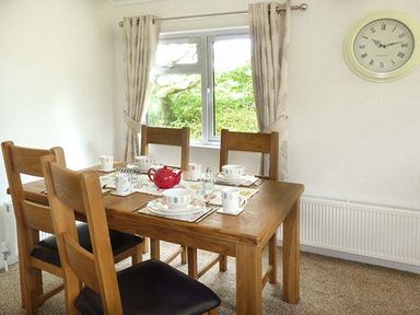 A dining room with a wooden table set for tea with cups and a red teapot at Chaffinch Lodge in Highampton near Sheepwash