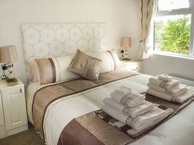 A bedroom with a bed covered with brown and white bedding and folded towels on top at Chaffinch Lodge in Highampton near Sheepwash