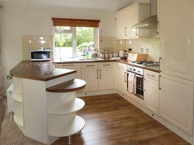A kitchen with cream cabinets wooden countertops a window with a wooden blind and kitchen appliances at Chaffinch Lodge in Highampton near Sheepwash