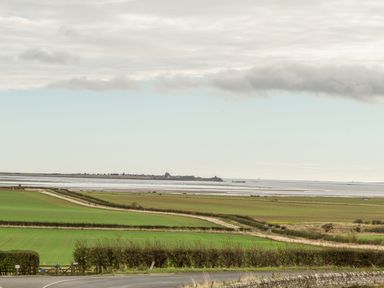 Farmland with hedges near a coastal area with an expanse of water and an island in the distance at St Cuthberts Cottage in Beal near Holy Island